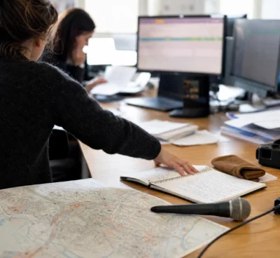 Journaliste préparant un sujet politique dans une rédaction française avec carnet, carte papier et micro de presse