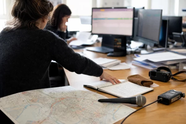 Journaliste préparant un sujet politique dans une rédaction française avec carnet, carte papier et micro de presse