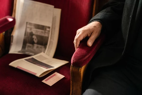 Main posée sur un fauteuil rouge de théâtre, avec un billet et un programme culturel flous sur un siège voisin