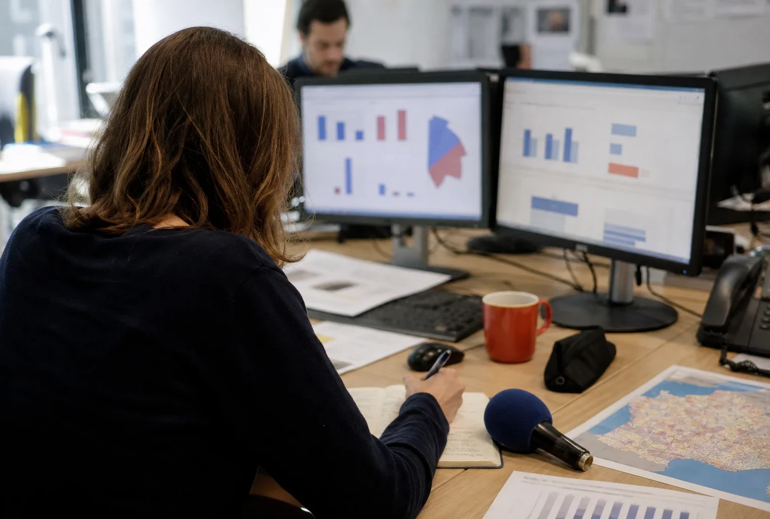 Journaliste préparant un sujet sur la présidentielle 2027 dans une rédaction locale, avec carnet et micro sans logo