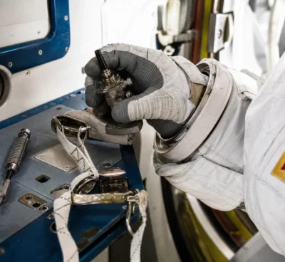 Main gantée vérifiant un connecteur d’antenne et un câble de sécurité lors de la préparation d’une sortie spatiale