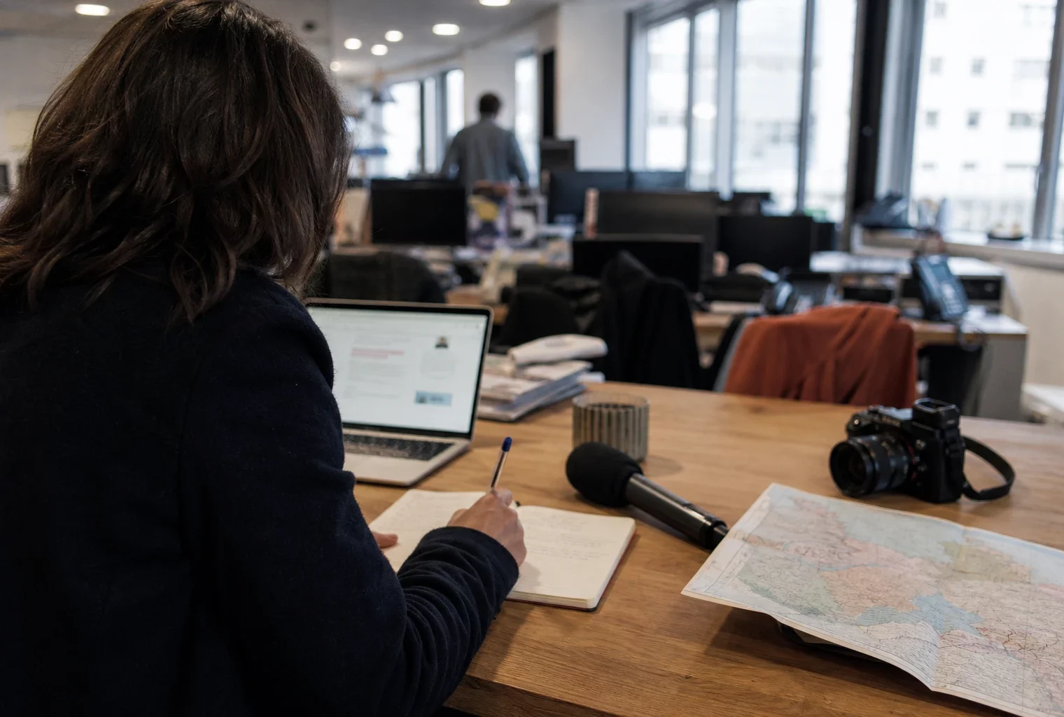 Journaliste préparant un sujet politique local dans une rédaction de Dijon, avec carnet, carte floue et micro de presse