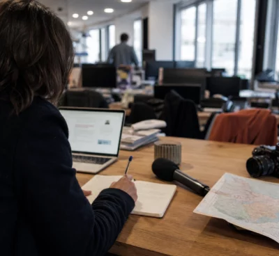 Journaliste préparant un sujet politique local dans une rédaction de Dijon, avec carnet, carte floue et micro de presse