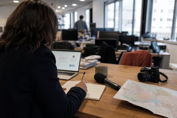 Journaliste préparant un sujet politique local dans une rédaction de Dijon, avec carnet, carte floue et micro de presse