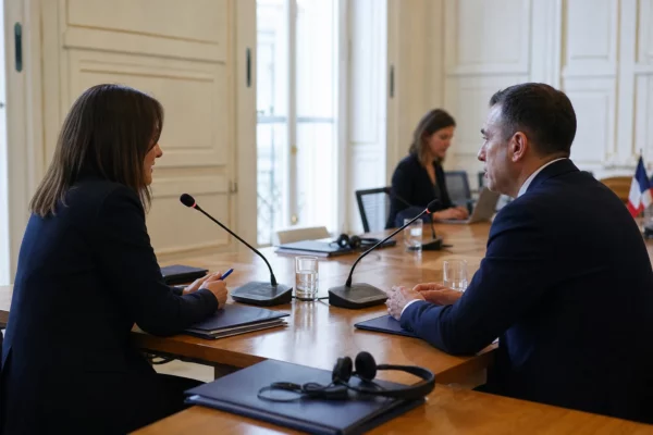 Table de négociation institutionnelle avec micros, dossiers et silhouettes anonymes dans une salle lumineuse française.