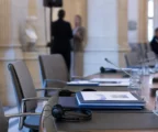 Table de négociation européenne avec casques audio, dossiers, verres d’eau et mini-drapeaux discrets, scène diplomatique réaliste.