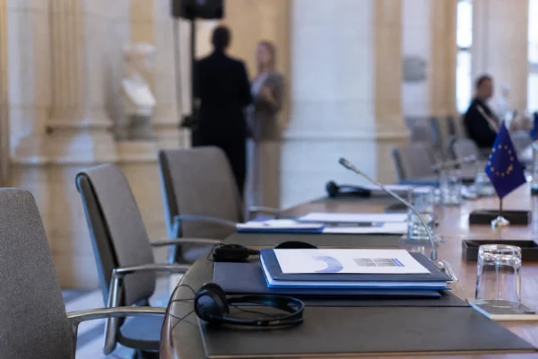 Table de négociation européenne avec casques audio, dossiers, verres d’eau et mini-drapeaux discrets, scène diplomatique réaliste.