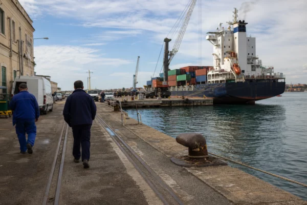 Quai maritime français avec dockers et habitants anonymes, illustrant les tensions commerciales autour du détroit d’Ormuz