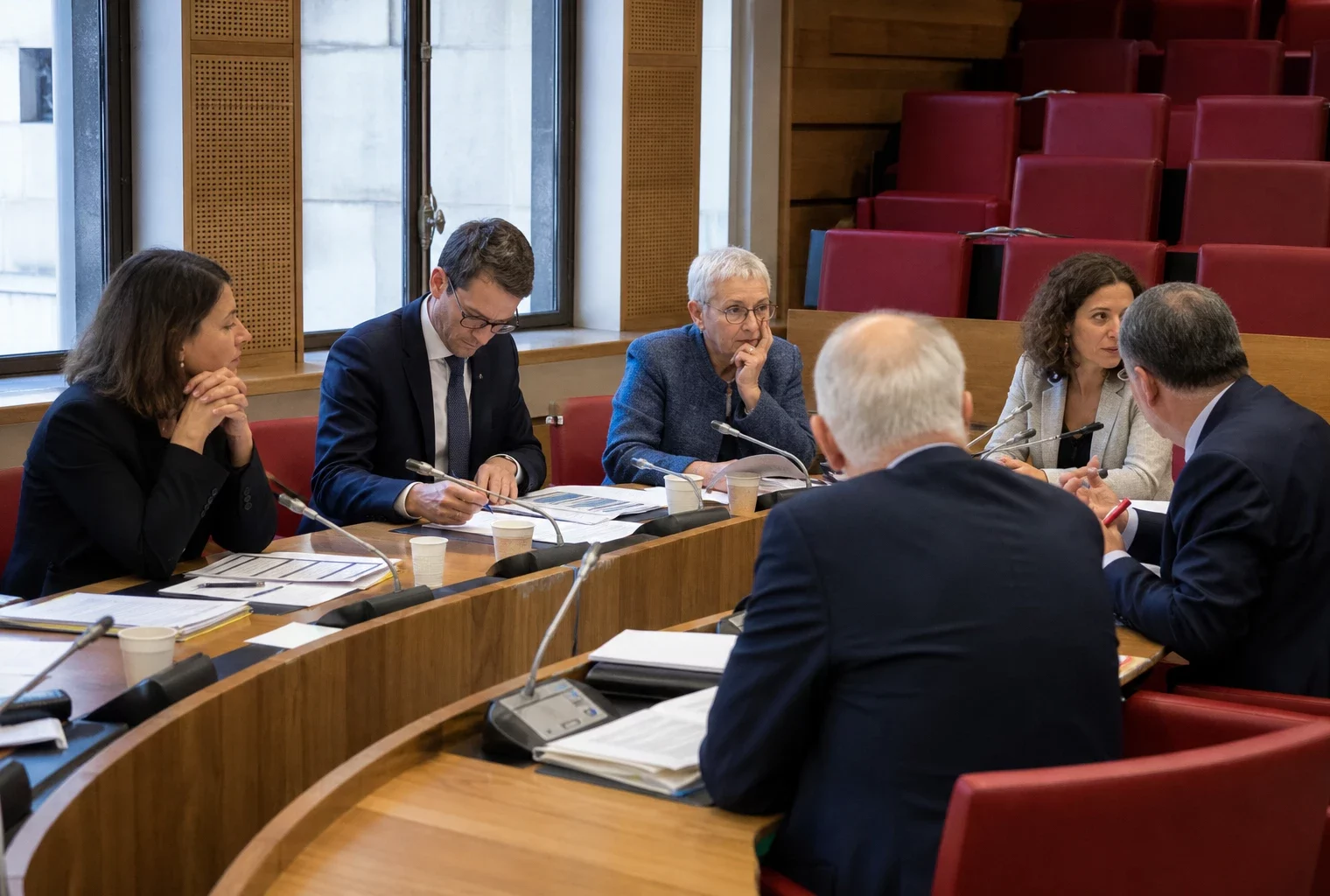 Commission parlementaire française où des élus anonymes débattent autour de micros et de dossiers, dans une salle éclairée