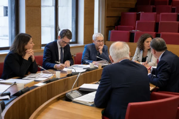 Commission parlementaire française où des élus anonymes débattent autour de micros et de dossiers, dans une salle éclairée