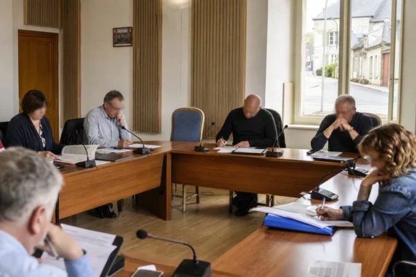 Salle de conseil municipal française avec une chaise vide, des micros et des dossiers lors d’un débat migratoire