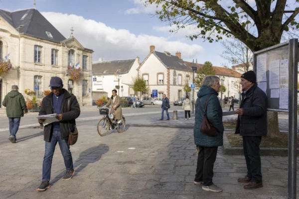 Rue d’une ville moyenne française où des habitants anonymes échangent près d’un équipement municipal