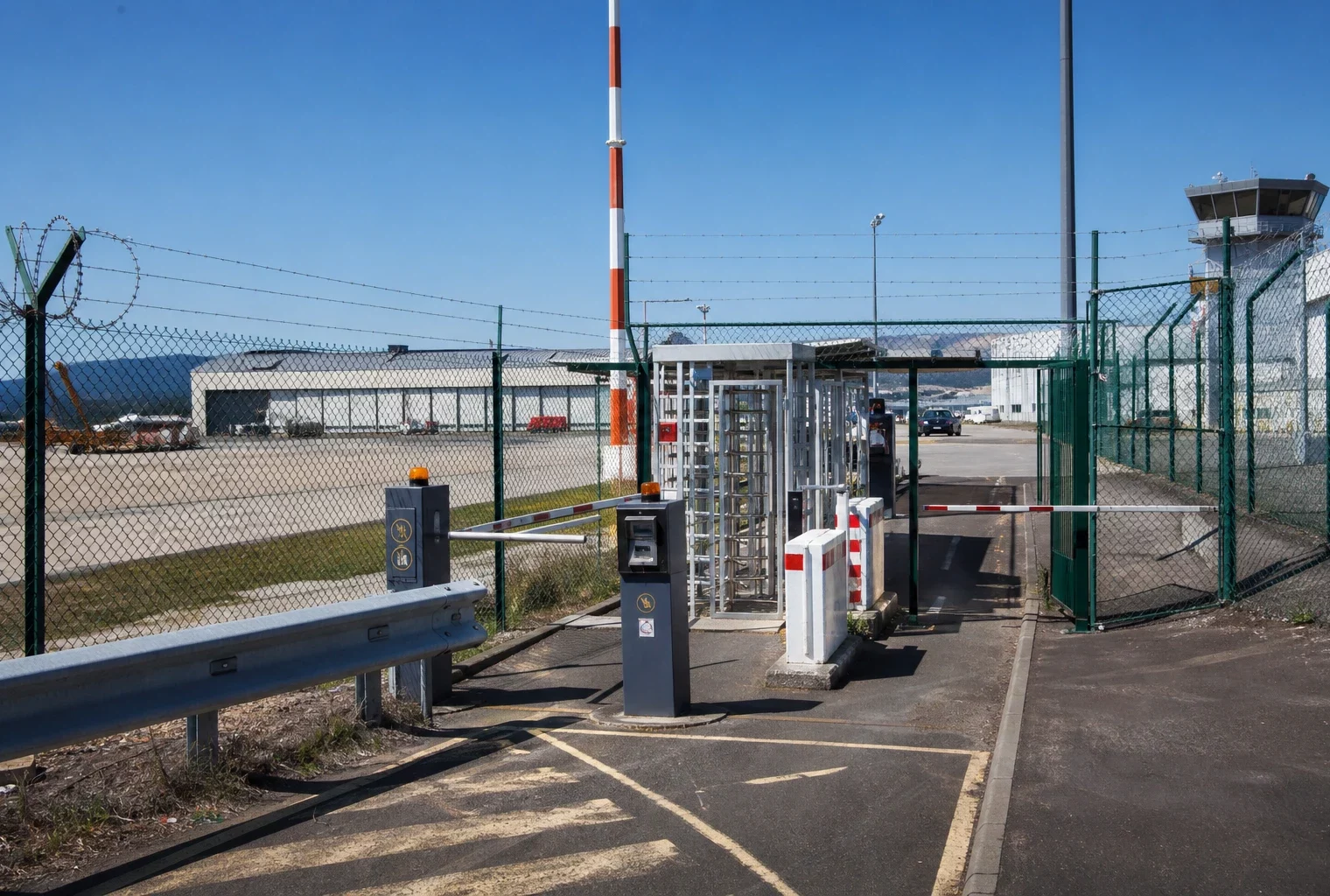 Dispositif de sécurité à l’entrée d’un aéroport français, avec grillage, accès contrôlé et zone technique en arrière-plan.