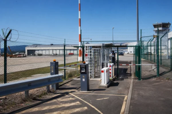 Dispositif de sécurité à l’entrée d’un aéroport français, avec grillage, accès contrôlé et zone technique en arrière-plan.