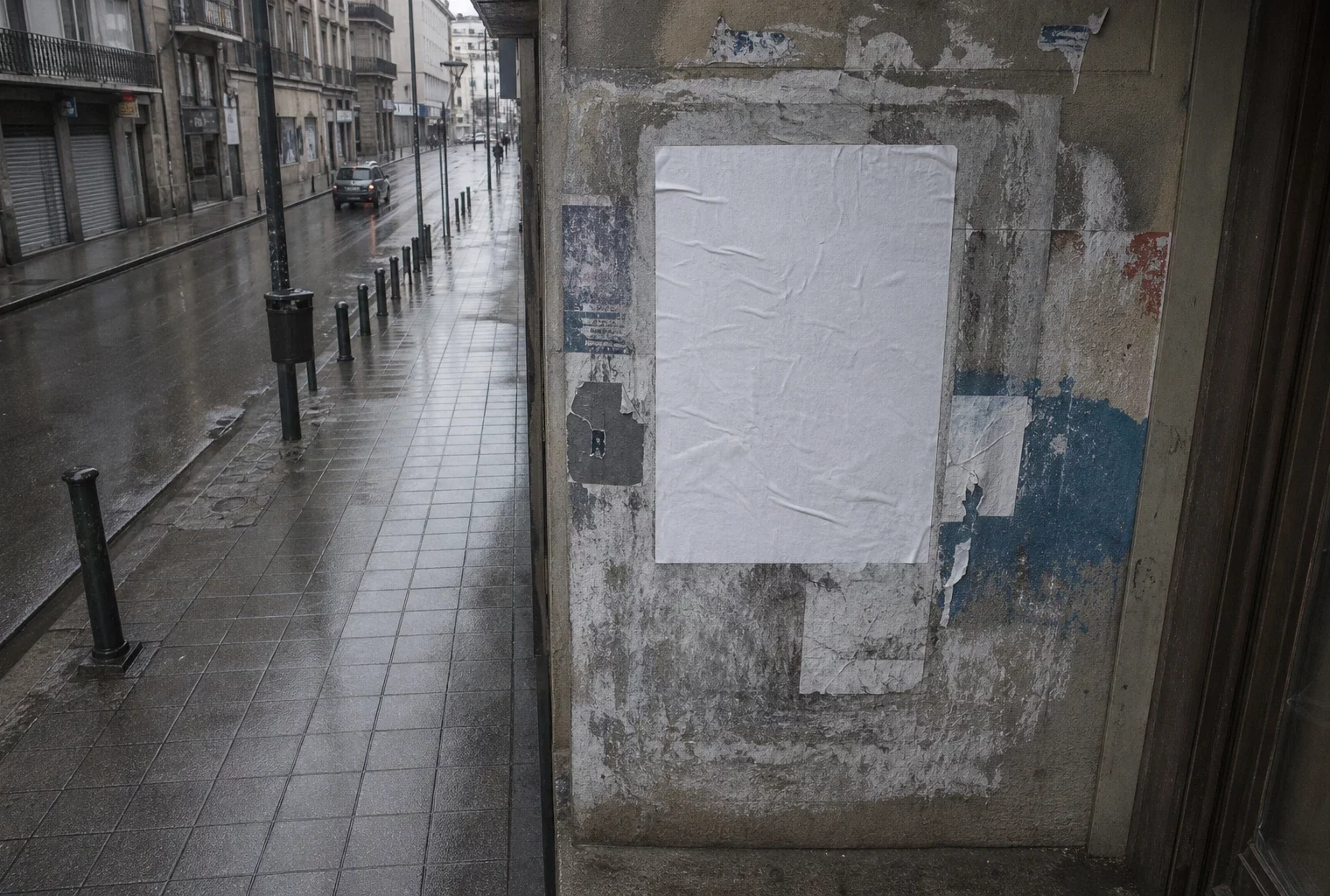 Affiche électorale municipale froissée sur un support urbain, dans une rue de province mouillée et grise, vue en plongée.