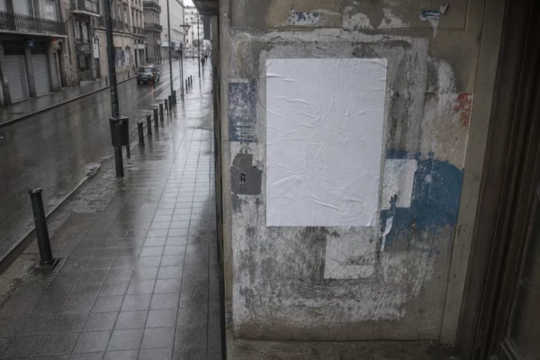 Affiche électorale municipale froissée sur un support urbain, dans une rue de province mouillée et grise, vue en plongée.