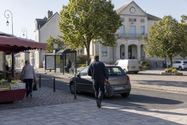 Travailleur rejoignant sa voiture sur une place de commune française, symbole des trajets quotidiens en zone rurale