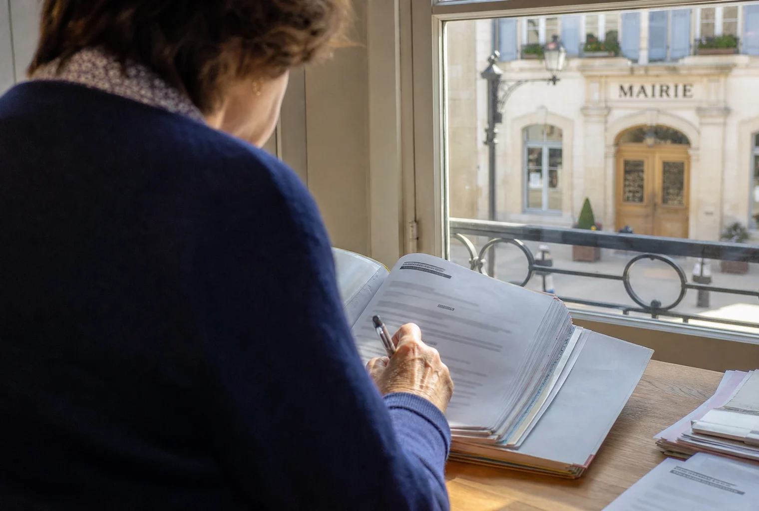 Élu local anonyme prenant des notes sur un dossier dans une mairie française lumineuse