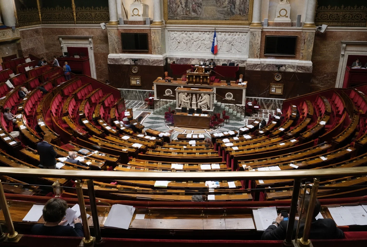 L’hémicycle de l’Assemblée nationale vu en plongée, vide et lumineux, avec sièges en arc et pupitres au premier plan.