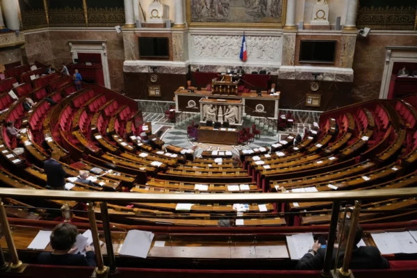 L’hémicycle de l’Assemblée nationale vu en plongée, vide et lumineux, avec sièges en arc et pupitres au premier plan.