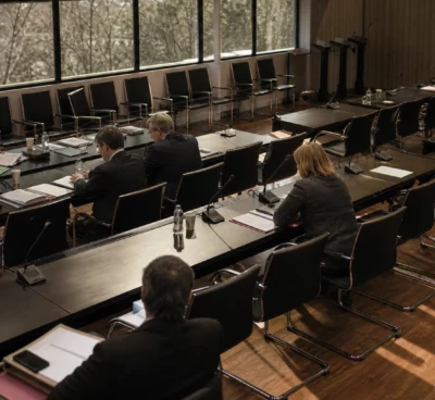 Salle de réunion parlementaire à l’Assemblée nationale, tables alignées, micros et dossiers, lumière d’hiver rasante.