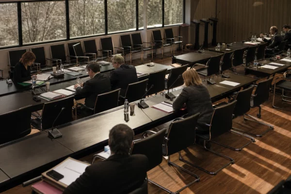 Salle de réunion parlementaire à l’Assemblée nationale, tables alignées, micros et dossiers, lumière d’hiver rasante.