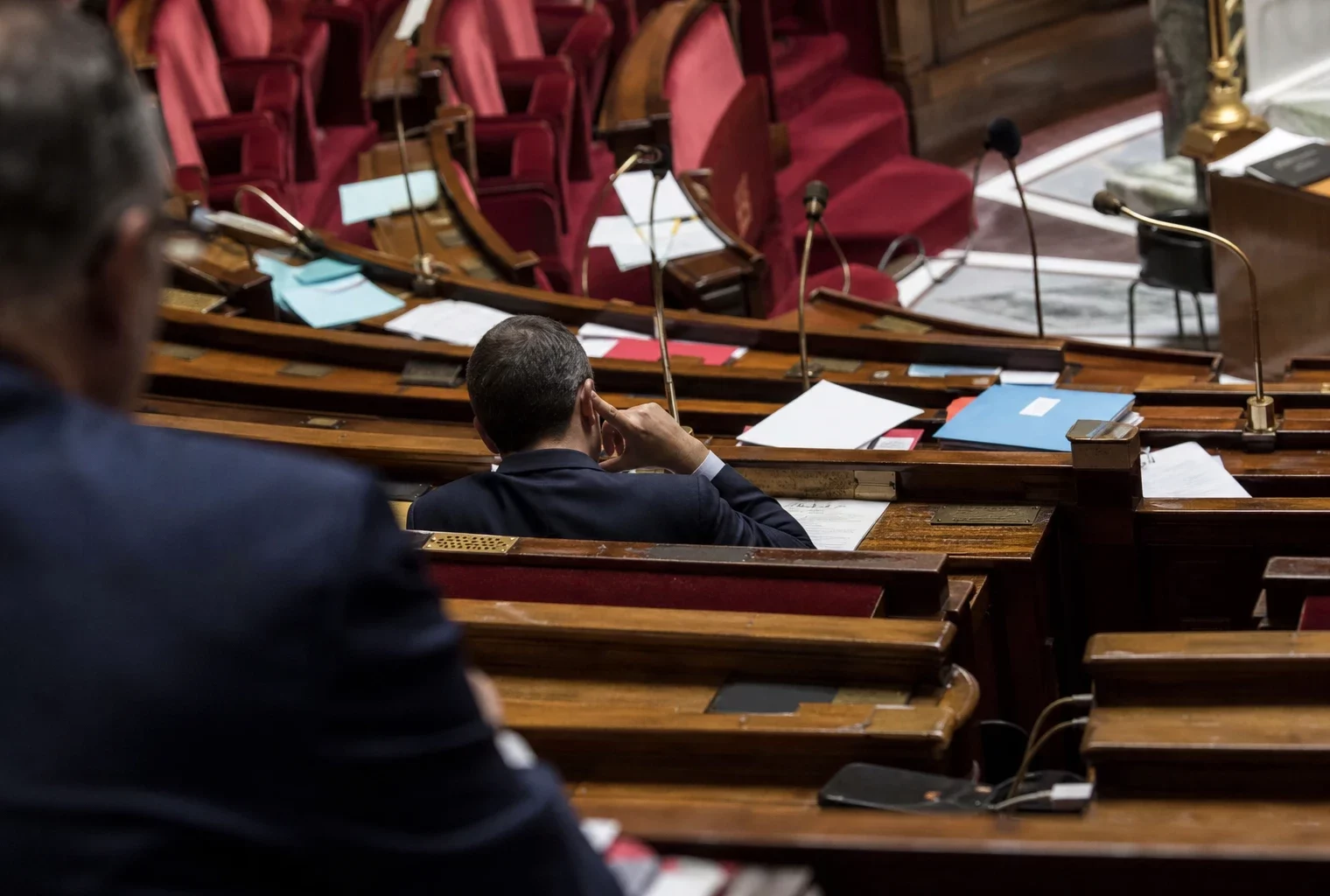 L’hémicycle de l’Assemblée nationale avec ses pupitres et micros, cadre sobre pour un sujet politique et judiciaire.