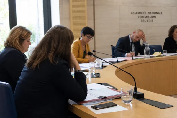 Audition parlementaire montrant des personnes anonymes autour de micros et de dossiers dans une salle publique française