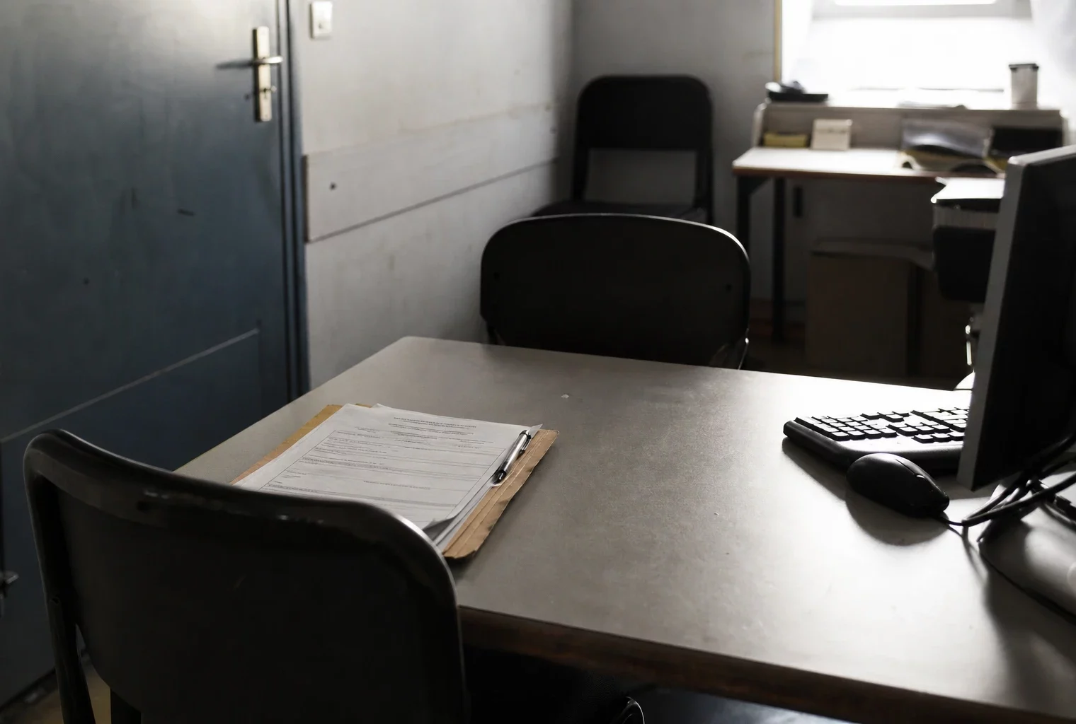 Salle d’audition d’un commissariat avec table, chaises et dossier de plainte, pour une enquête après violences sexuelles.
