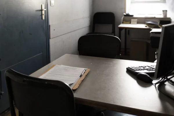 Salle d’audition d’un commissariat avec table, chaises et dossier de plainte, pour une enquête après violences sexuelles.