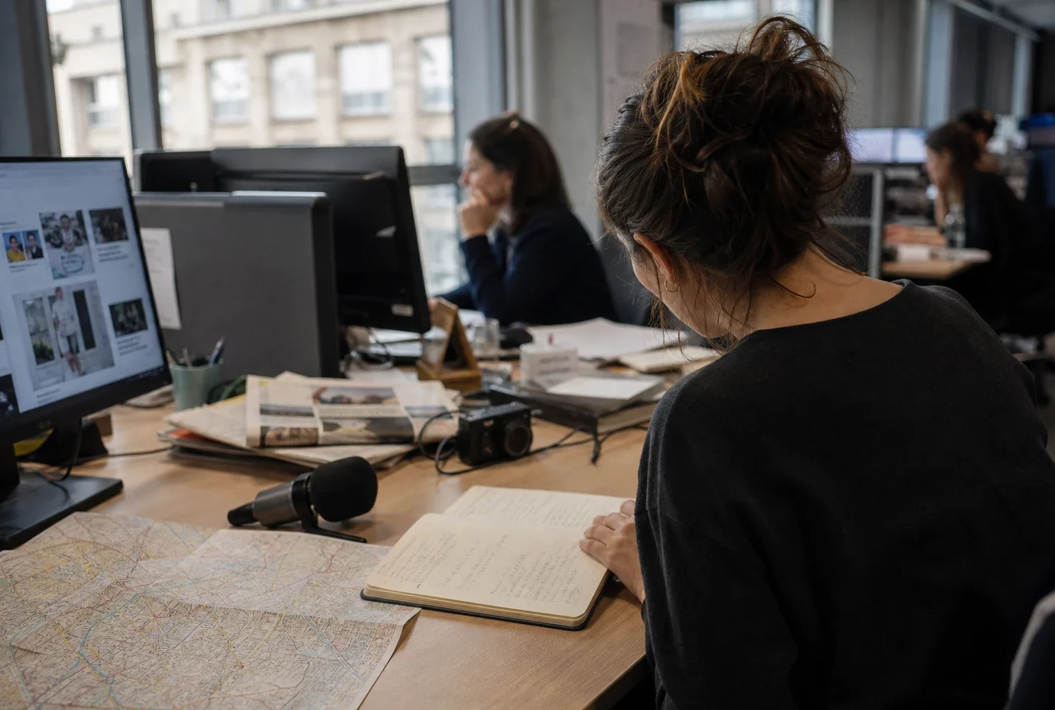 Journaliste préparant un sujet politique dans une rédaction locale française, avec carnet, carte de Paris et micro de presse