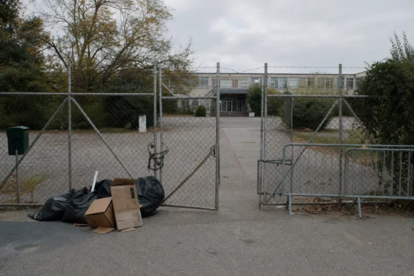 Grilles d’un lycée public fermées et barrées, avec sacs et cartons devant l’entrée, façade en arrière-plan.