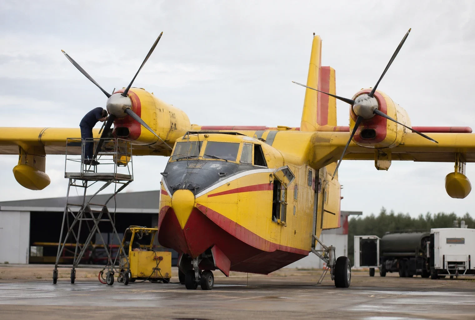 Un bombardier d’eau de la Sécurité civile stationné sur une base aérienne, avec du matériel de maintenance autour.
