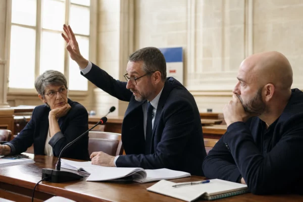 Débat parlementaire sur le budget 2027 dans une salle publique, avec main levée, micro et documents juridiques flous