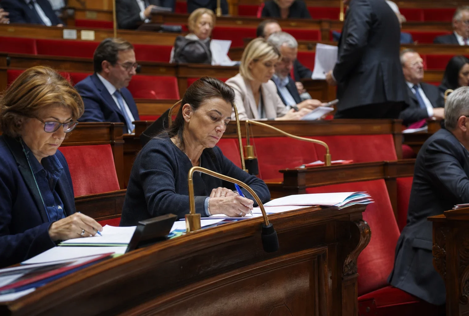 Dans l’hémicycle de l’Assemblée nationale, des pupitres et dossiers évoquent le débat budgétaire sur l’aide à l’Ukraine.
