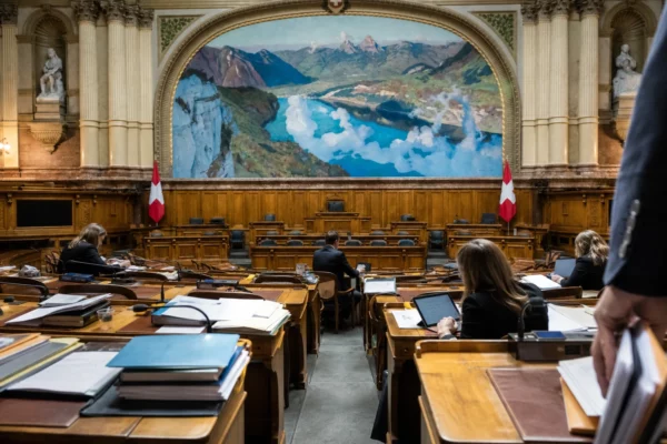 Salle de commission parlementaire vide avec pupitres, dossiers budgétaires et micros sous une lumière grise et humide.