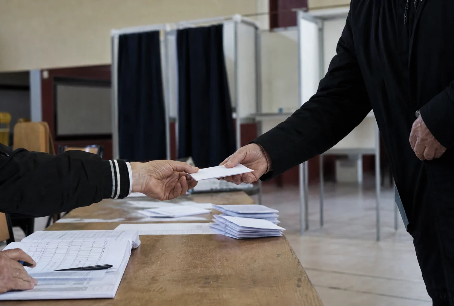 Salle de vote pour une primaire, avec table d’émargement, bulletins et isoloirs dans une salle municipale.