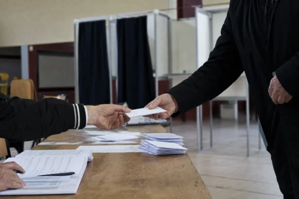 Salle de vote pour une primaire, avec table d’émargement, bulletins et isoloirs dans une salle municipale.