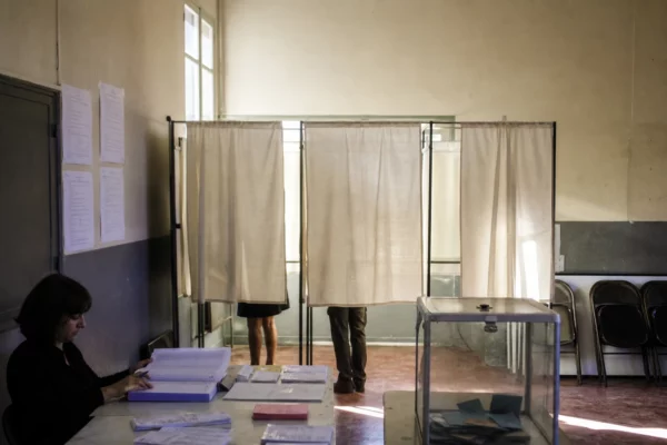 Salle de vote avec isoloirs, table d’émargement et urne pour une primaire de la gauche.