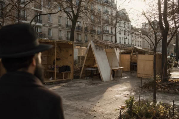 Cabanes de Souccot en bois dans une cour parisienne, avec branchages, tables simples et immeubles urbains en arrière-plan.