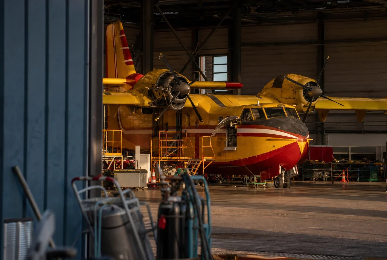 Un avion bombardier d’eau dans un hangar de maintenance, avec du matériel technique autour.