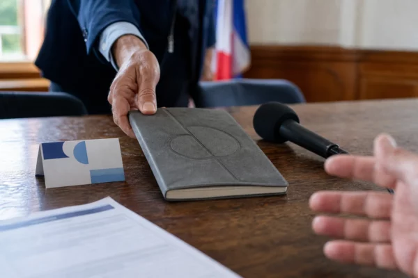 Main anonyme près d’un carnet de campagne et d’un micro de presse dans une salle municipale française