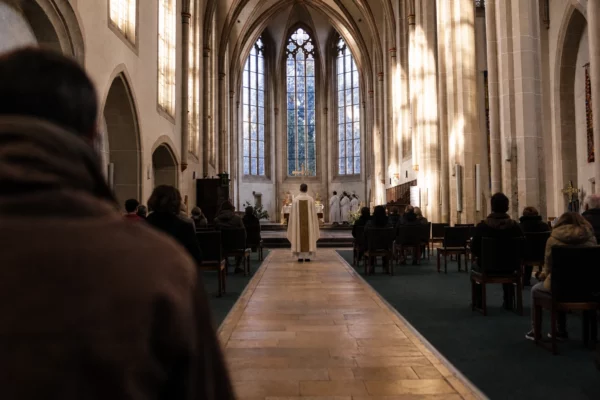 Intérieur de la cathédrale de Metz avec allée centrale, chaises éparses et quelques fidèles vus de dos sous une lumière d’hiver.