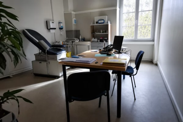 Une salle de consultation hospitalière simple, avec bureau, fauteuil médical et chaises, pour évoquer un centre d’accueil des victimes.