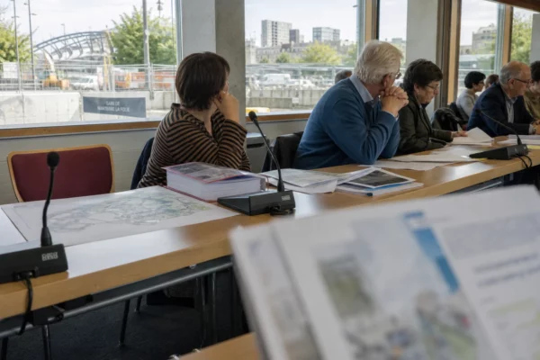 Salle municipale à Nanterre avec micros, dossiers et chaise vide, sur fond de chantier du futur métro
