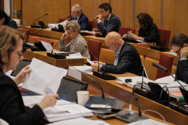 Salle de commission à l’Assemblée nationale avec micros et dossiers, où les députés examinent un texte sur les violences sexuelles.