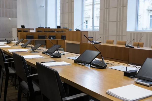 Salle de commission à l’Assemblée nationale, tables d’audition vides, micros et dossiers, vue plongeante lumineuse.