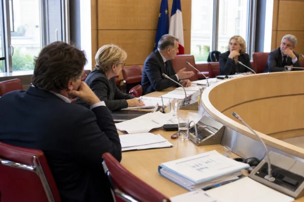 Réunion de commission parlementaire française avec élus anonymes, micros et dossiers sur une table claire