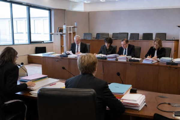 Salle de réunion judiciaire avec dossiers, micros de table et chaises alignées pour l’examen d’une plainte contre un ministre