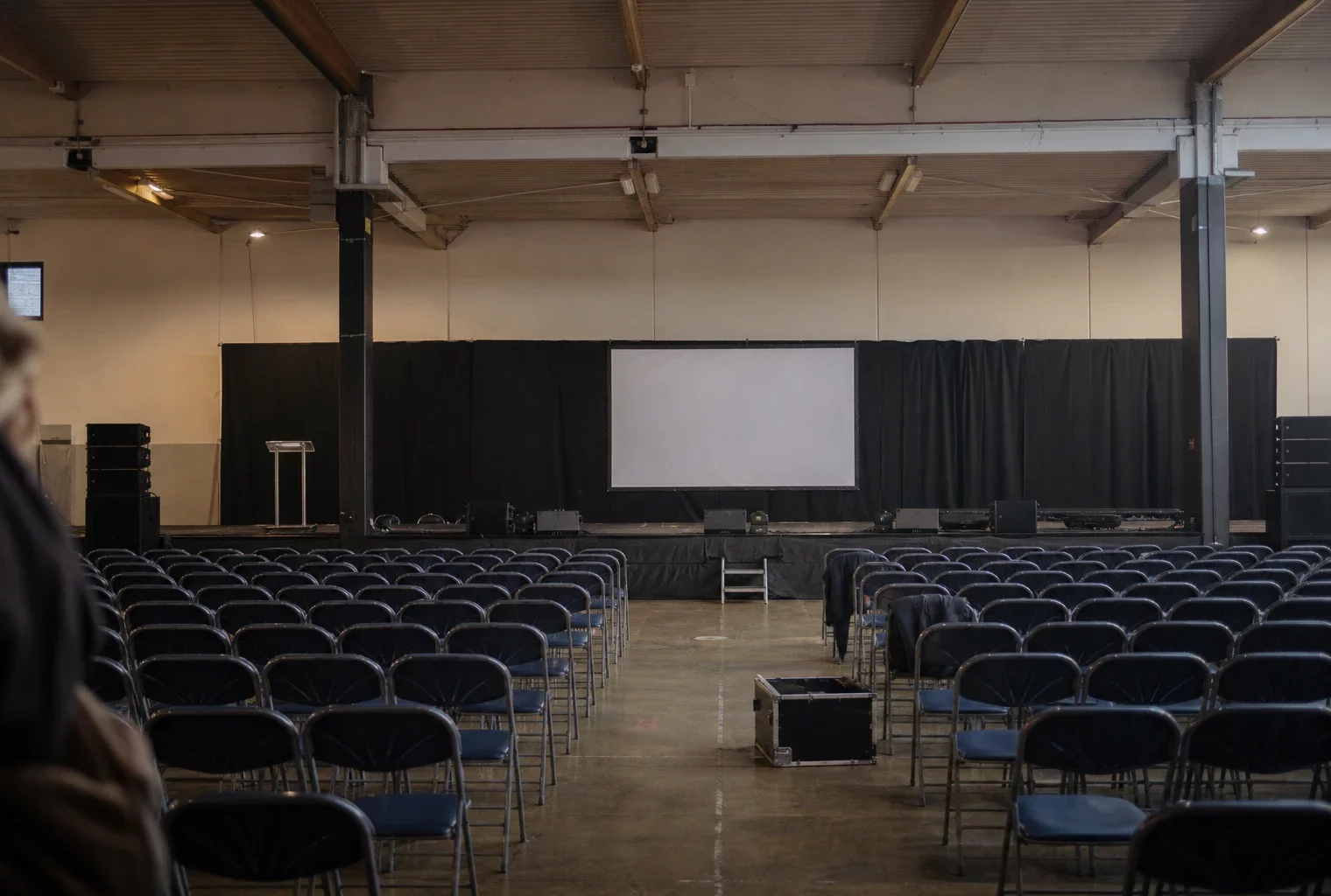 Salle de congrès à Orléans avec rangées de chaises, pupitre et estrade, prête pour un meeting politique.